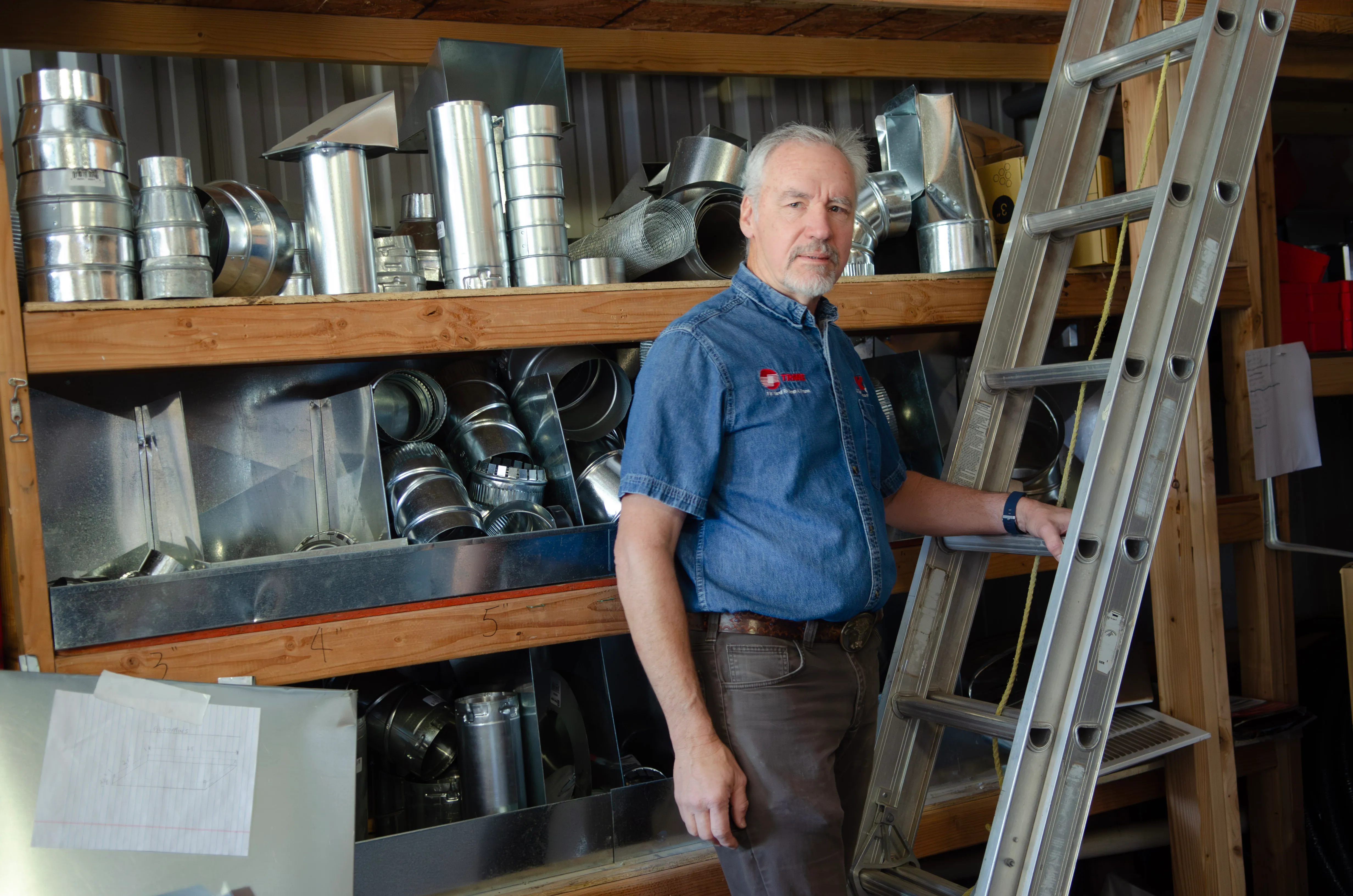 Karl Thomas standing by stocked ductwork and a ladder in the shop.
