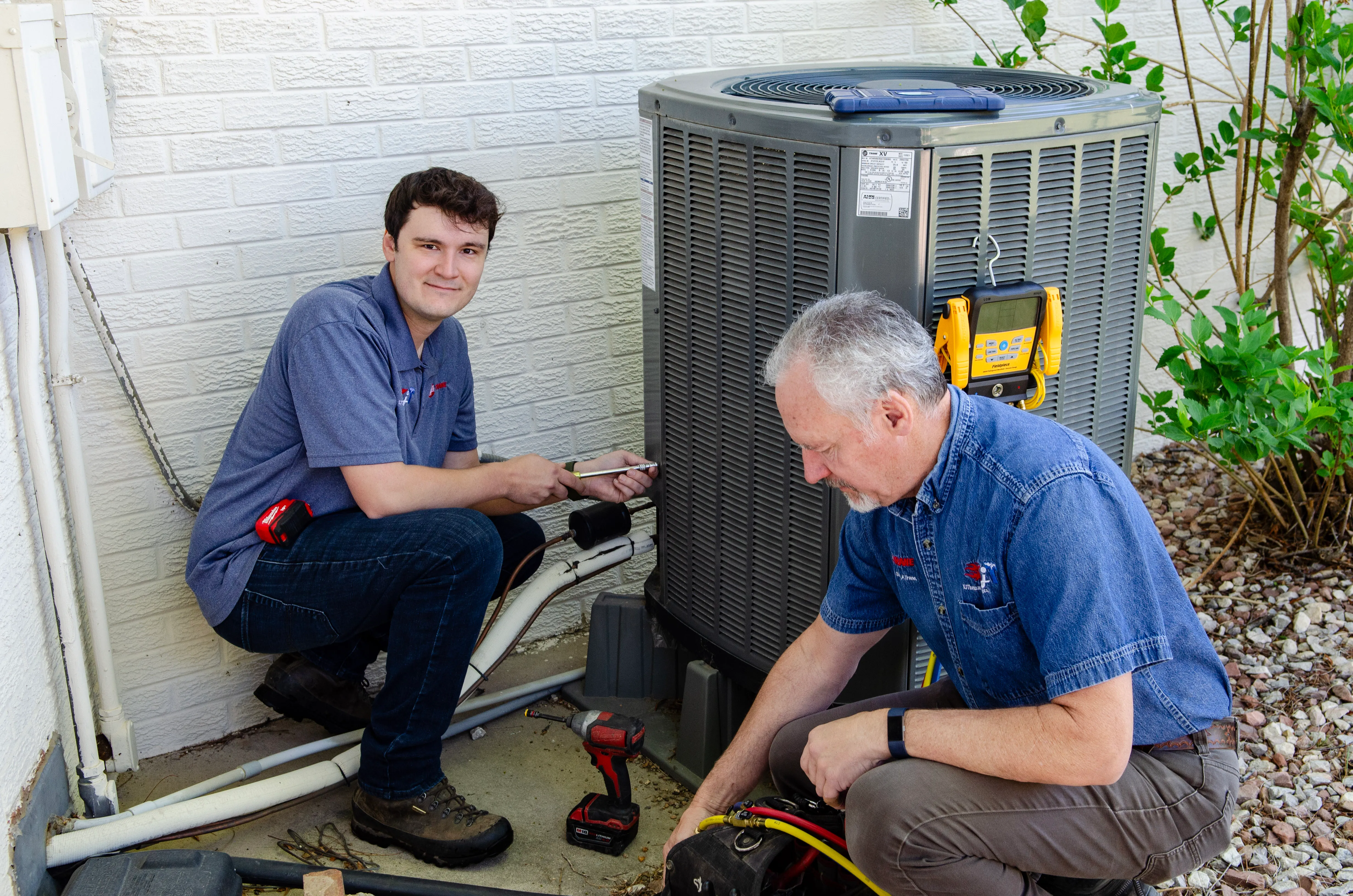Two KJ Thomas Mechanical team members servicing a heat pump outside a home.